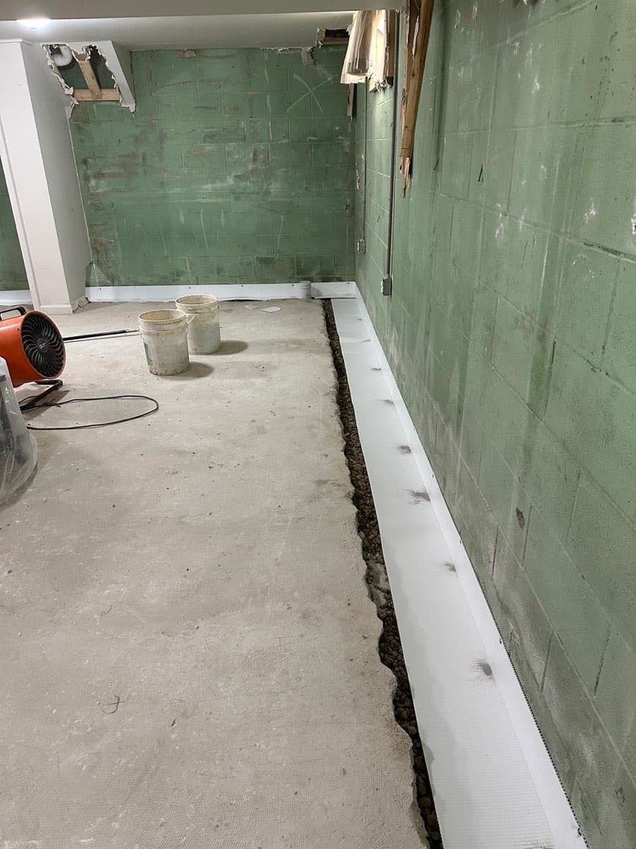 Interior perimeter drain along a block basement wall, washed stone in the trench and a flange at the base of the wall